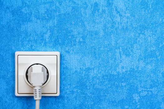 Electrical plug connected into the socket on blue wall
