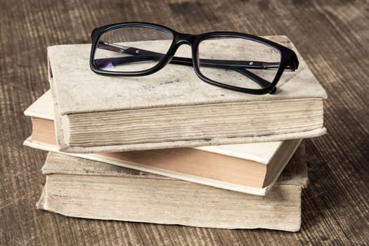 Stack of books and reading glasses on the wooden background.