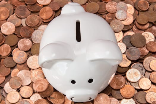 White piggy bank on pile of copper coins (Euro cents).Top view.