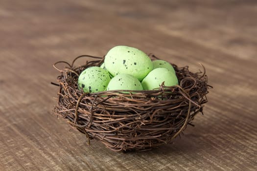 Decorative green eggs in nest on wooden background