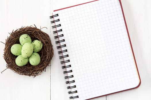 Nest with painted eggs and blank notebook for copy-space