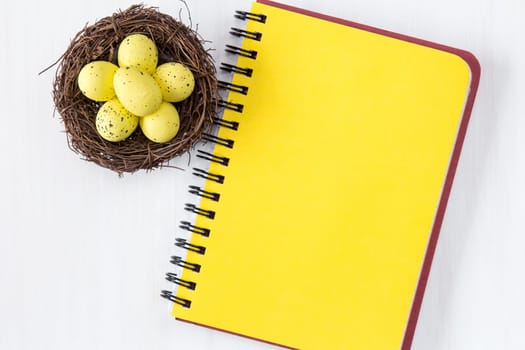 Nest with painted Easter Eggs and blank notebook for copy-space