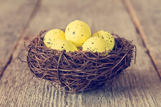 Decorative yellow eggs in nest on wooden background