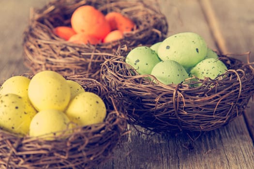 Three nests with painted eggs on wooden background. Close-up view with selective focus.