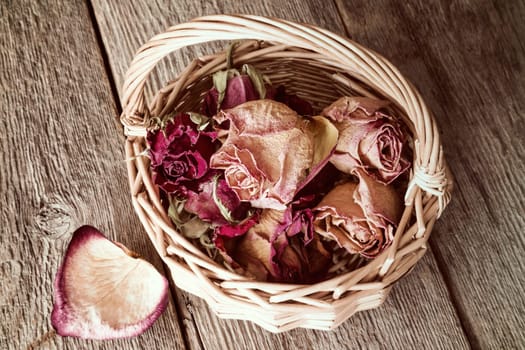 Buds of faded roses in wicker basket on wooden background