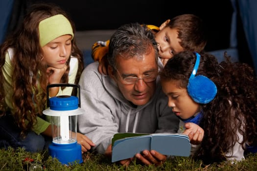 Senior man reading a book to his three grandchildren