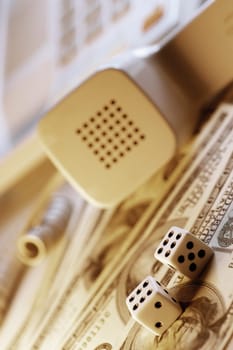 Telephone receiver and dice on top of United States hundred Dollar bills, close-up