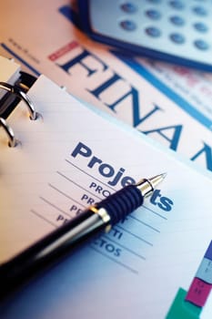 Pen, spiral notebook, planning list, financial section of newspaper and calculator, close-up