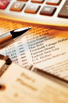 Calculator and pen on top of currency exchange rate information, close-up