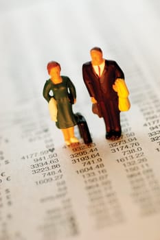 Toy businessman and businesswoman standing on top of paper with financial figures