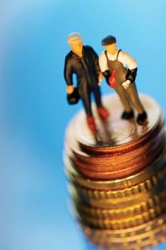 Two toy men on top of stack of coins, close-up