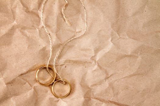 Two gold wedding rings tied with string over paper background