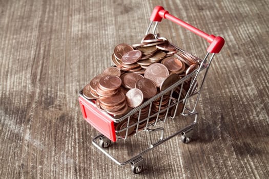 Shopping cart with Euro cent coins on wooden background