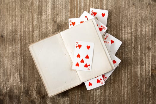 Open book and playing cards on wooden background