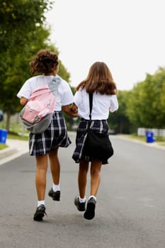 Rear view of two schoolgirls walking with holding hands