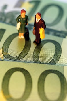 Toy businessman and businesswoman standing on top of Euro one hundred bank notes, close-up