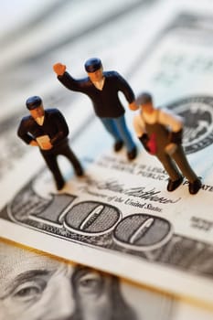 Three toy men standing on top of United States one hundred dollar bills, close-up