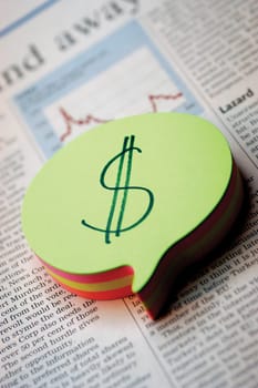 Notepad with dollar sign on it, on top of business section of newspaper, close-up