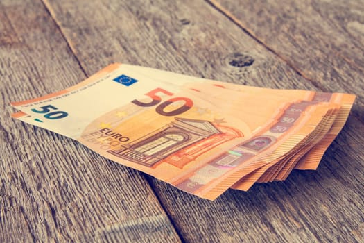 Bunch of fifty Euro banknotes on wooden background. Filtered image.