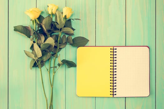 Blank notebook and three roses on the blue wooden background