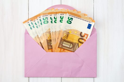 Pink envelope with Euro bills over wooden background