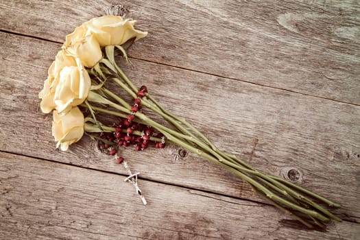 Silver crucifix and yellow roses on old wooden background