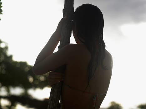 Rear view of a young woman holding a tree trunk