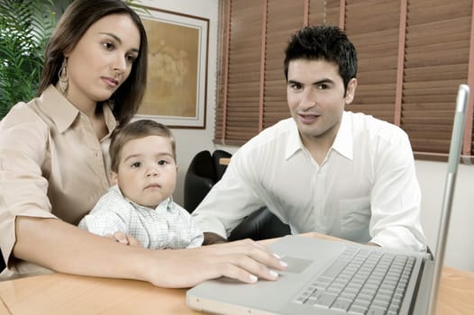 Portrait of a baby boy sitting in front of a laptop with his parents