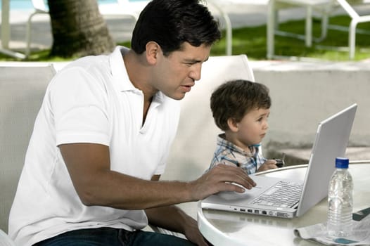 Side profile of a father working on a laptop with his son sitting beside him
