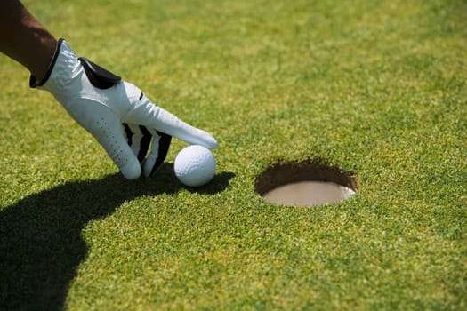 Close-up of a manŽs hand putting a golf ball near a hole