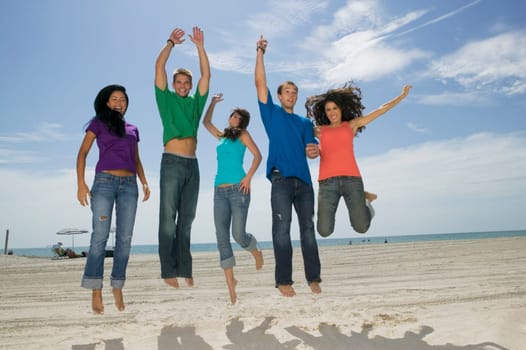 Low angle view of three young women and two young men jumping on the beach
