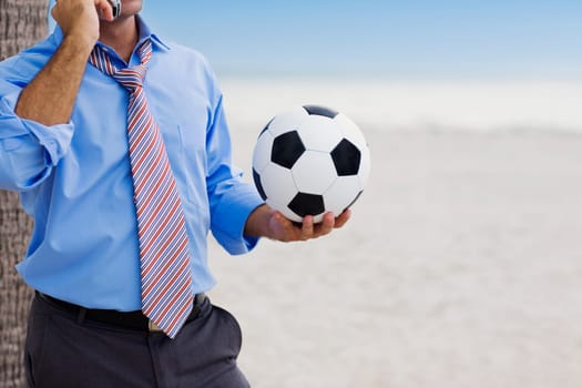 Mid section view of a man holding a soccer ball and talking on a mobile phone