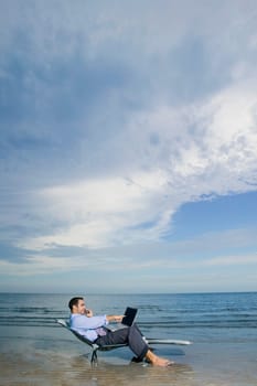 Side profile of a young man talking on a mobile phone and using a laptop
