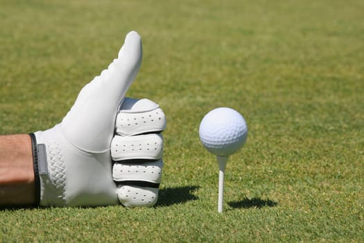Close-up of a personŽs hand making a thumbs up sign next to a golf ball on a tee