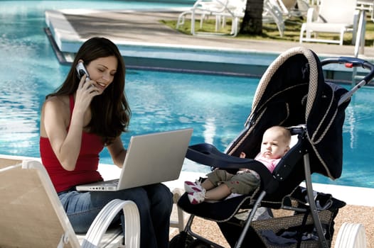 Mother talking on a mobile phone with her daughter beside her at the poolside