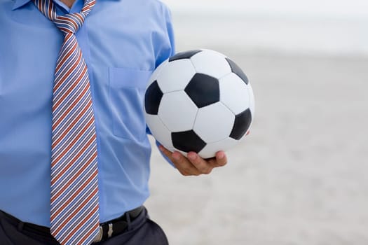 Mid section view of a man standing on the beach and holding a soccer ball