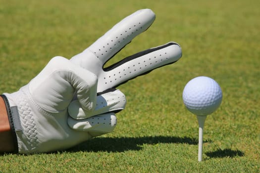 Close-up of a personŽs hand showing two fingers next to a golf ball on a tee