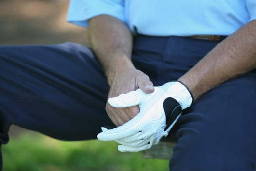 Mid section view of a man sitting on the bench wearing a golf glove