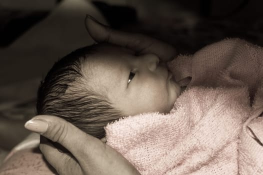 Beautiful Newborn baby boy closeup (6 days old) lying in mother lap in prenatal hospital. Kid wrapped in baby blanket (warm clothing) smiling and looking. His mother consoling and resting her baby.