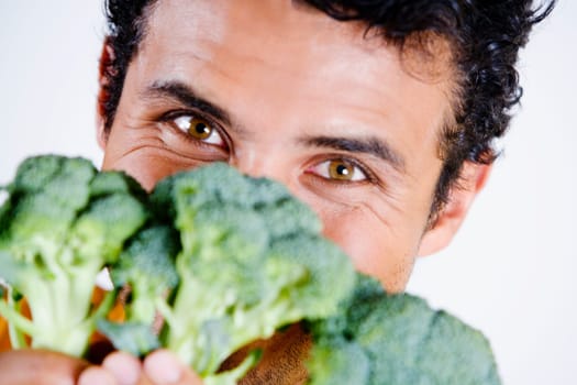 Portrait of a young man holding broccoli in front of his face