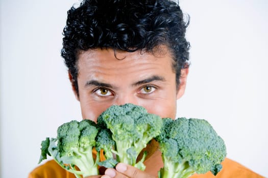 Portrait of a young man holding broccoli in front of his face