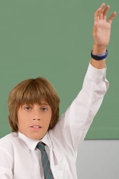 Portrait of a schoolboy with his hand raised in a classroom