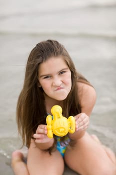 Portrait of a girl kneeling on the beach and holding a toy