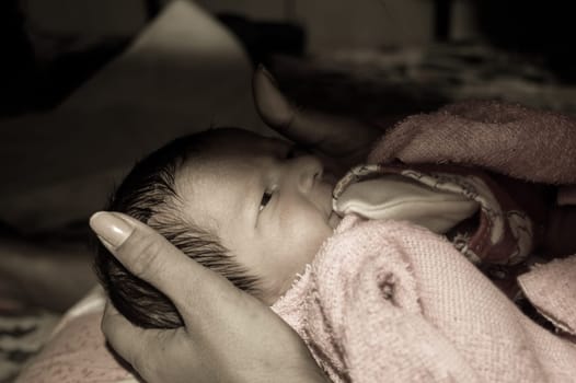 Beautiful Newborn baby boy closeup (6 days old) lying in mother lap in prenatal hospital. Kid wrapped in baby blanket (warm clothing) smiling and looking. His mother consoling and resting her baby.