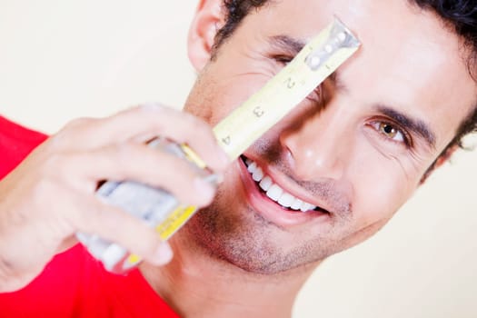 Portrait of a young man holding a measuring tape in front of his face and smiling