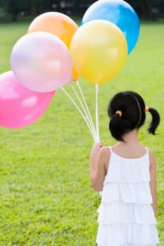 Rear view of a girl holding balloons in a park