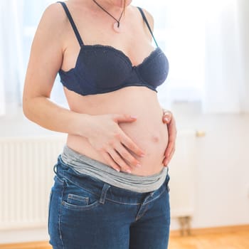 Close up of pregnant Caucasian mother touching her naked tummy
