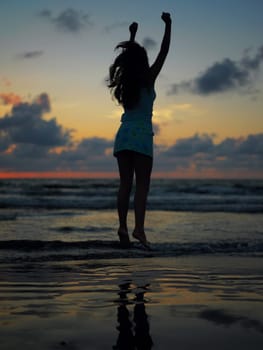 Silhouette of a teenage girl jumping on the beach at dusk