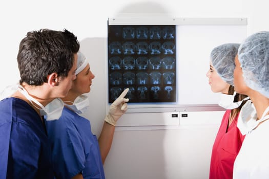 Side profile of a male surgeon and three female surgeons looking at a MRI scan