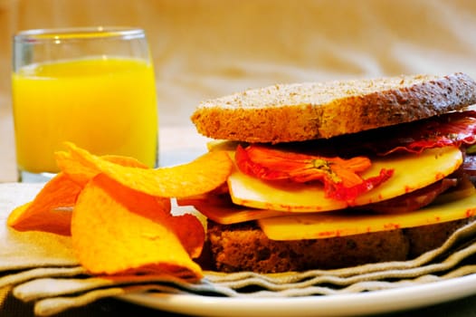 Close-up of orange juice with a sandwich and potato chips